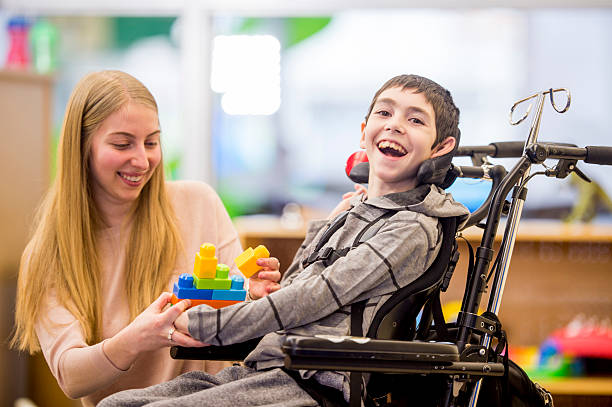 Happy Little Boy Playing with Toys A caregiver is helping a young boy with a physical disability play with plastic block toys. physical disability stock pictures, royalty-free photos & images