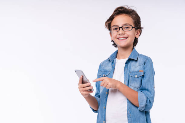 Happy little child pointing at smart phone isolated over white background Happy little child pointing at smart phone isolated over white background boys glasses stock pictures, royalty-free photos & images