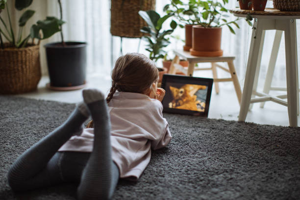 Happy little girl enjoying while watching cartoons on touchpad at home. stock photo