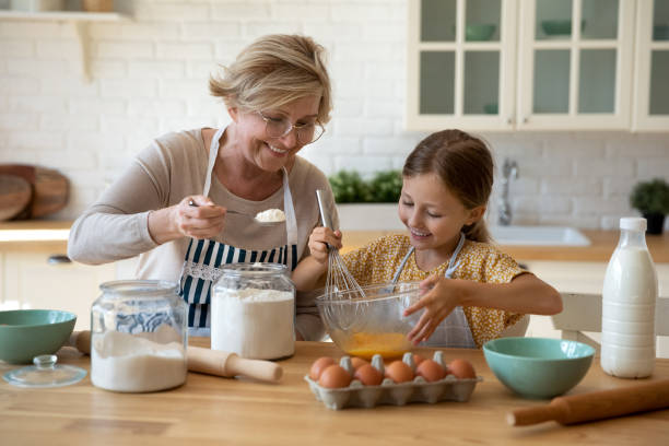 Happy little girl help senior grandma at kitchen mix dough stock photo