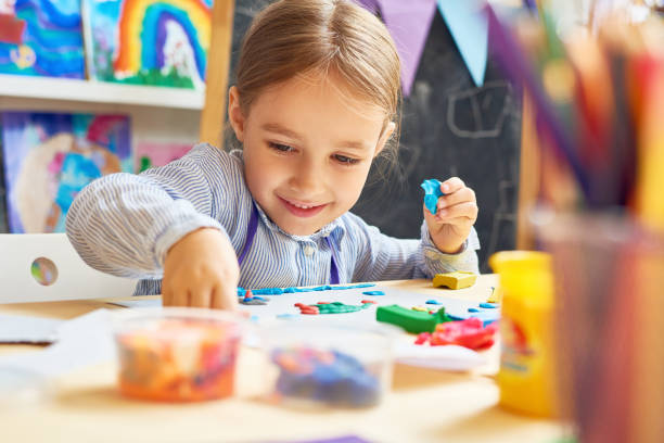 Happy Little Girl in Development School Portrait of smiling little girl working with plasticine in art and craft class of development school studio workplace photos stock pictures, royalty-free photos & images