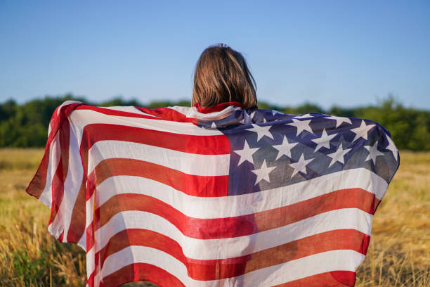 счастливая маленькая девочка-патриотка бежит в поле с американским флагом. - july 4 стоковые фото и изображения