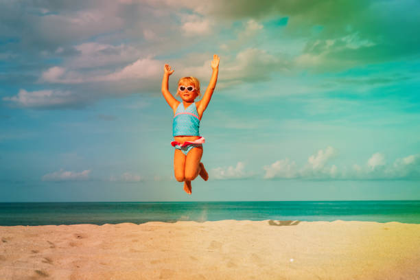 happy little girl play jump at beach happy little girl play jump at tropical beach little girls in bathing suits stock pictures, royalty-free photos & images