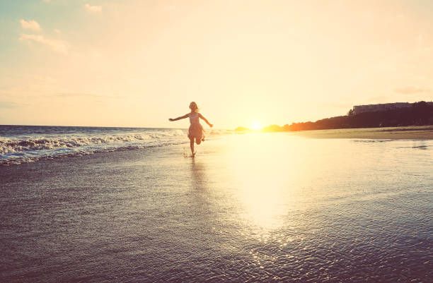 szczęśliwa dziewczynka biegająca wewnątrz wody na plaży o zachodzie słońca - dziecko bawiące się w wakacje - koncepcja młodości, stylu życia i szczęścia - filtr vintage - skupienie się na sylwetce - england australia zdjęcia i obrazy z banku zdjęć