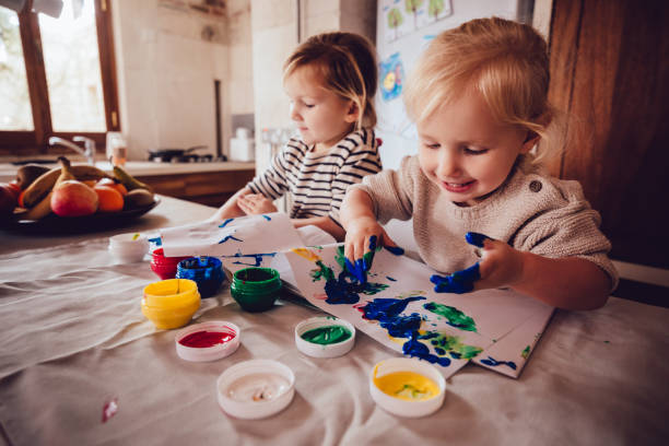 Happy little girls drawing with paint in family house kitchen stock photo