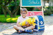 Glückliche kleine Kind Junge mit Brille sitzen durch Schreibtisch und Rucksack oder Umhängetasche