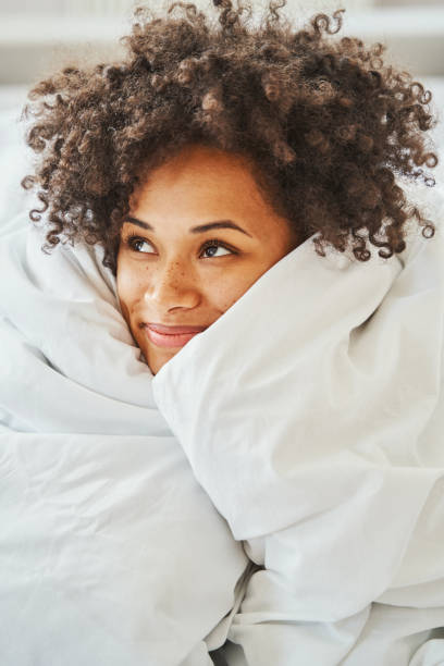 Happy lovely curly-headed lady daydreaming in her bed stock photo