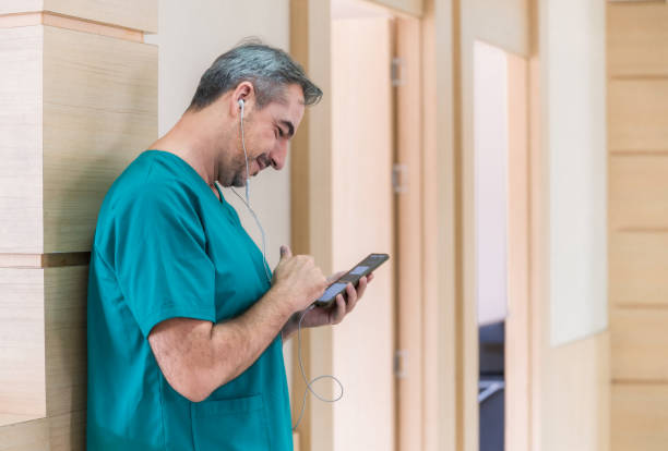 Happy male doctor wearing green surgeon dress standing with using mobile phone and text messaging in hospital. stock photo