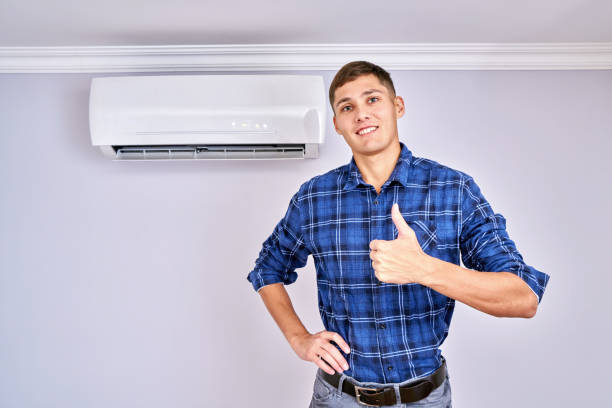 Happy male master in blue shirt installed air conditioner indoors and is happy with his job, showing thumb up and smiling stock photo