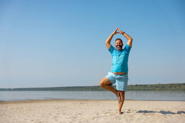 Happy man doing yoga in tree pose on the beach on a clear day stock photo