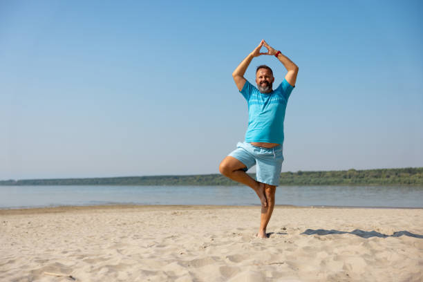 Happy man exercising on the beach, keeping balance on one leg, arms above head stock photo
