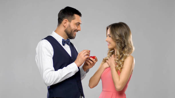 happy man giving engagement ring to woman couple, proposal and engagement concept - happy man giving diamond ring in little red gift box to woman over grey background fiancé stock pictures, royalty-free photos & images