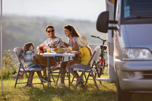 Happy man playing a guitar to his family during camping day by the trailer. stock photo