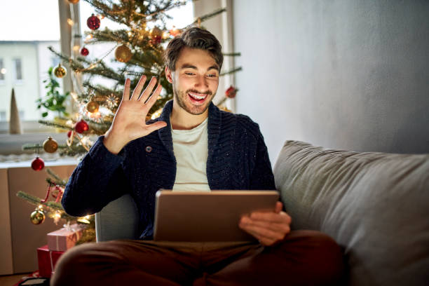 Happy man waving during Christmas video call staying in touch with friends and family stock photo