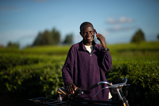 Happy African Man with a bicycle looking at camera talking on a mobile phone in a rural setting in Southern Malawi Africa