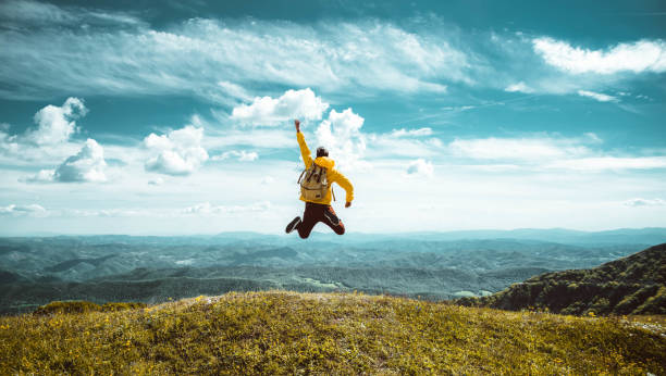 Happy man with open arms jumping on the top of mountain - Hiker with backpack celebrating success outdoor - People, success and sport concept stock photo