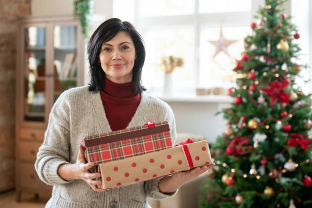 gelukkig rijpe donkerbruine wijfje in casualwear holding stapel giftboxes - vrouw kerstboom versieren stockfoto's en -beelden