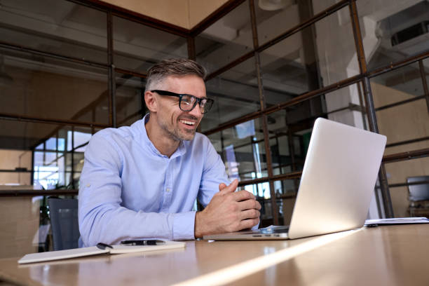 Happy mature business man looking at laptop having virtual meeting in office. stock photo