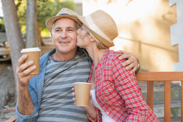 Happy mature couple drinking coffee on a bench in the city Happy mature couple drinking coffee on a bench in the city on a sunny day 50 59 years stock pictures, royalty-free photos & images