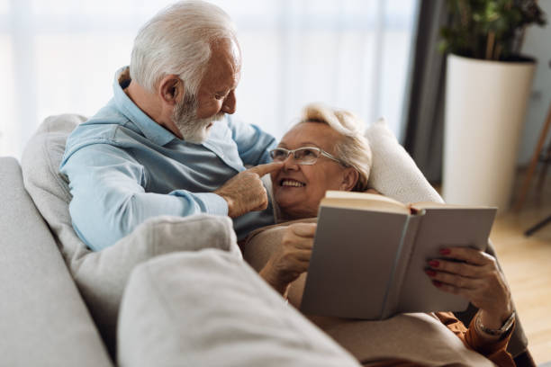 Happy mature couple in love talking while reading a book  at home stock photo