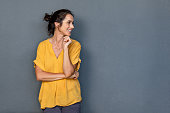 Mature beautiful latin woman isolated on grey background looking on side with copy space. Portrait of positive brunette woman smiling and looking away. Happy middle aged lady standing against grey wall and thinking.