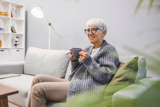 Happy mature woman relaxing on the sofa with a warm beverage at home stock photo