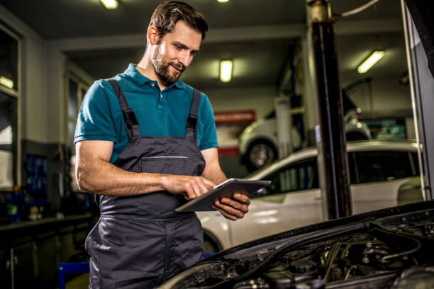 Happy mechanic examining car diagnostics on digital tablet in auto repair shop. stock photo