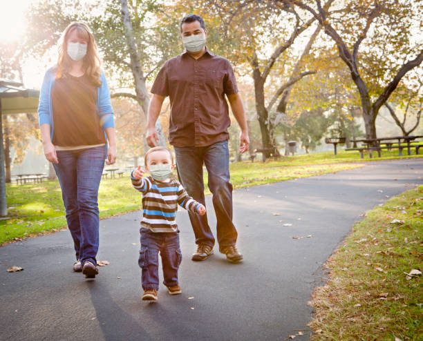 familia étnica de raza mixta feliz caminando en el parque usando máscara facial médica - máscara protectora fotografías e imágenes de stock