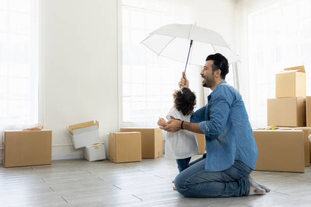 Happy moment family. Father and daughter relax in living room holding the white umbrella. Just moving new house many parcel box on the floor. stock photo