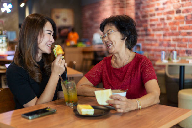 Happy mother and daughter enjoying teatime in cafe Senior asian woman having afternoon tea with her daughter, they are talking happily in a coffeeshop asian mother talking with daughter stock pictures, royalty-free photos & images