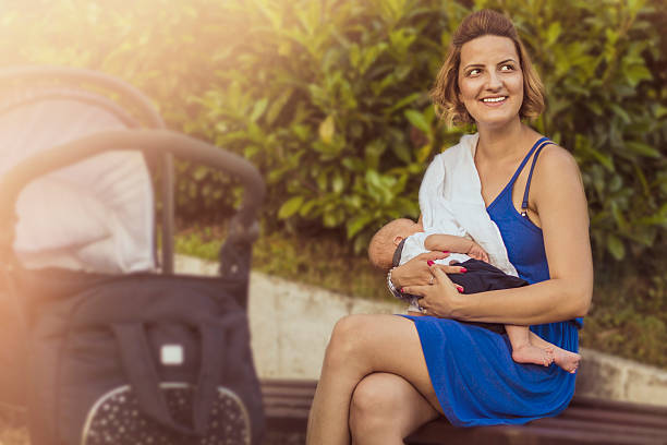 Happy mother breastfeeding her newborn baby in public on sunlight Happy mother breastfeeding her newborn baby in public on sunlight increase breast milk stock pictures, royalty-free photos & images