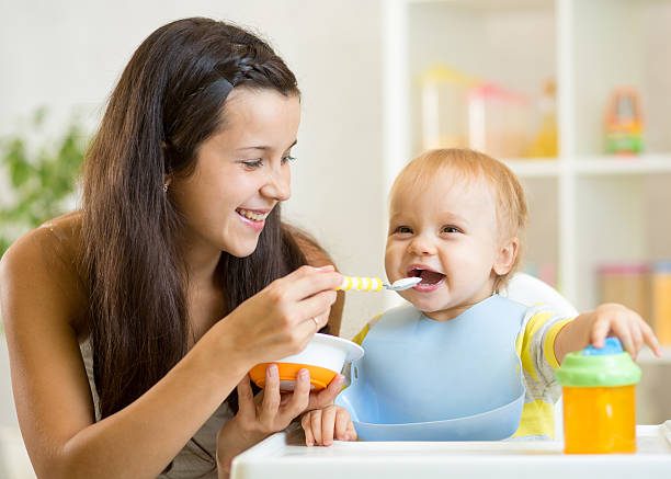 Happy mother spoon feeding her baby child stock photo