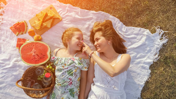 Happy mother touches daughter nose lying on picnic blanket stock photo