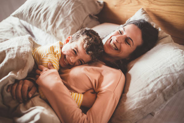 Happy mother with little son in bed in the morning Happy young mother having fun and embracing little son in bed in the morning tickling beautiful women pictures stock pictures, royalty-free photos & images
