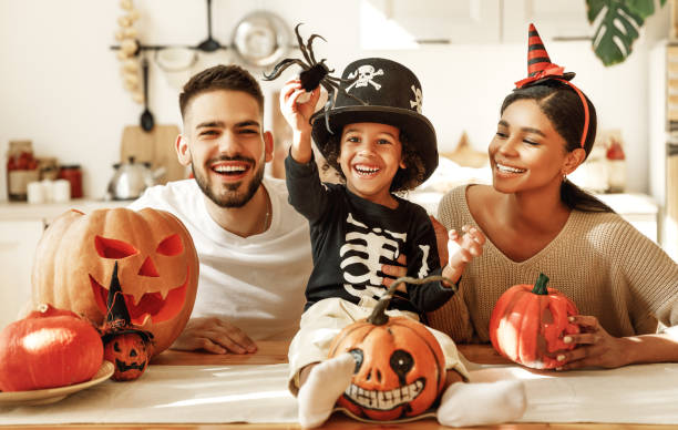 Happy multi ethnic family preparing for Halloween celebration Cheerful multi ethnic family parents with son smiling  while creating jack o lantern from pumpkin during Halloween celebration in kitchen at home costume photos stock pictures, royalty-free photos & images