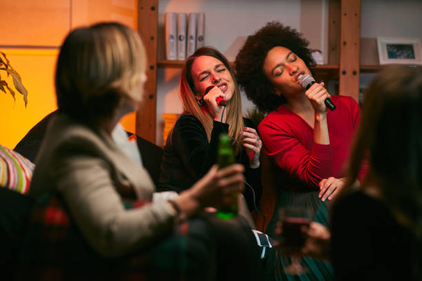 Happy multicultural friends sitting at home, laughing, singing, and having fun on karaoke night. stock photo