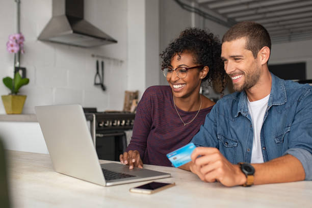 Happy multiethnic ouple making online payment Smiling young couple making shopping online with credit card and laptop at home. Happy multiethnic couple holding debit card while buying on ecommerce site using laptop. Cheerful guy and african girl making online purchase. electronic banking stock pictures, royalty-free photos & images