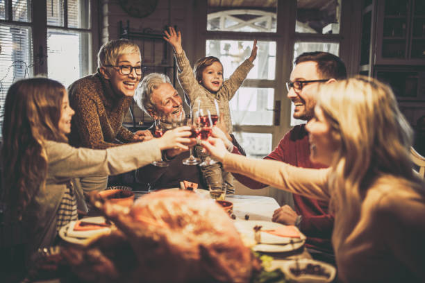 happy multi-generation familj rosta samtidigt ha thanksgiving lunch i matsalen. - family dinner bildbanksfoton och bilder