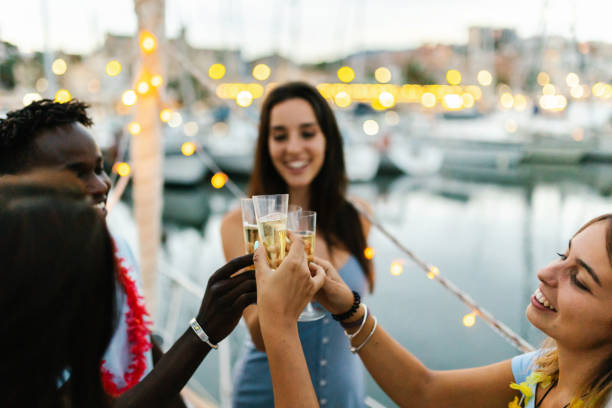 Happy multiracial young people cheering with champagne on a boat during christmas holidays - Millennial friends celebrate birthday together - Friendship, eve and celebration concept stock photo