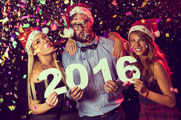 Three young friends having fun at New Year's Eve Party, holding...