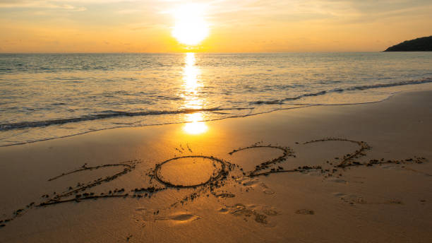 Happy New Year 2022, Lettering on the beach with waves and sunset sky Numbers 2022 year on the seashore, Message hand written in the golden sand on beautiful sunset or sunrise golden sky background stock photo