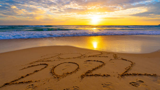 Happy New Year 2022, Lettering on the beach with waves and sunset sky Numbers 2022 year on the seashore, Message hand written in the golden sand on beautiful sunset or sunrise golden sky background. stock photo