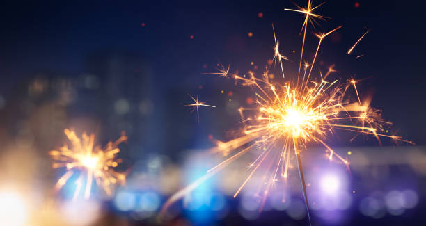feliz año nuevo, brillante destello ardiente contra fondo de luz de la ciudad borrosa - fireworks fotografías e imágenes de stock