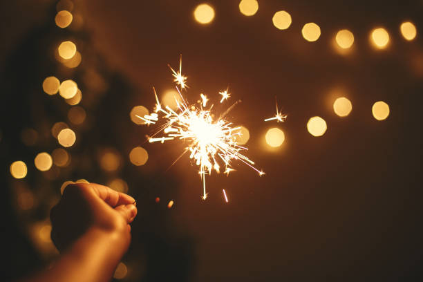 Happy New Year. Glowing sparkler in hand on background of golden christmas tree lights, celebration in dark festive room. Space for text.   Fireworks burning in hand. Happy Holidays Happy New Year. Glowing sparkler in hand on background of golden christmas tree lights, celebration in dark festive room. Space for text.   Fireworks burning in hand. Happy Holidays new years eve girl stock pictures, royalty-free photos & images