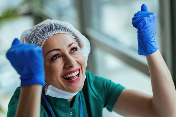 Happy nurse with raised hands celebrating good news at the hospital. Young female doctor with hands raised feeling excited and looking up while working at medical clinic. relief carving stock pictures, royalty-free photos & images