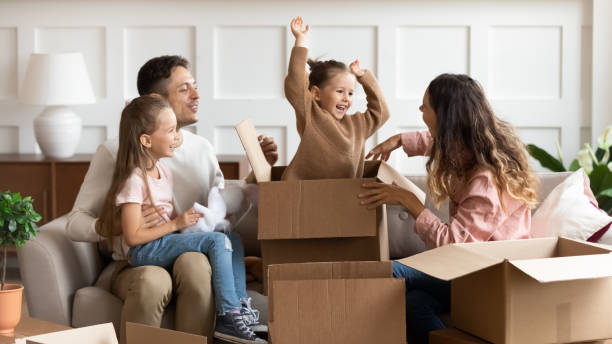 Happy parents and children playing on moving day unpacking boxes Happy family parents and children tenants renters new home owners playing on moving day unpacking boxes, cute little child daughter jump out of box enjoying relocation into own house concept relocation stock pictures, royalty-free photos & images