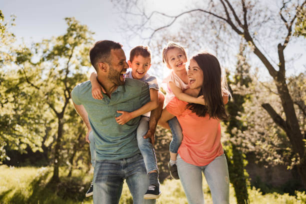 Happy parents having fun while piggybacking their small kids in nature. stock photo