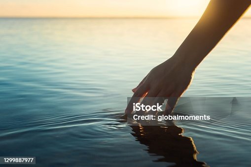 istock Happy people in nature. A woman feeling and touching the ocean water during sunset. 1299887977