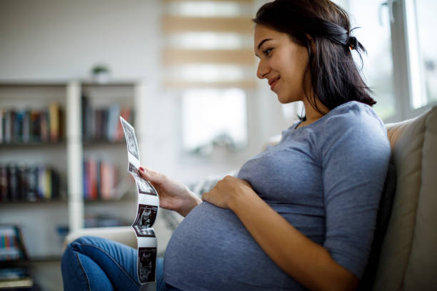 Happy pregnant woman looking at ultrasound scan at home stock photo