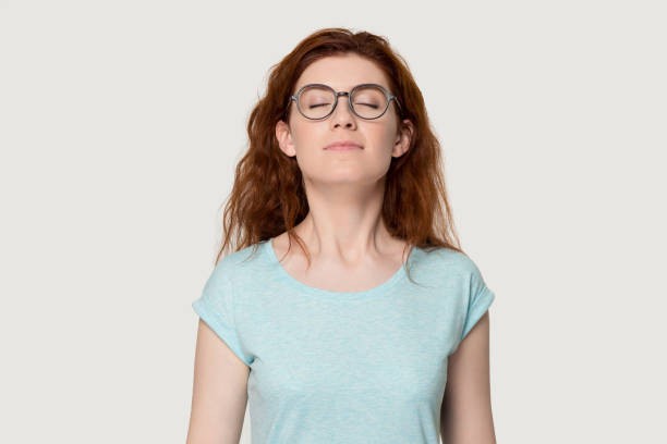Happy red-haired girl breathe fresh air enjoying smell Happy young redhead woman in glasses feel calm breathe fresh air managing stress practicing exercises, peaceful red-haired girl in eyewear isolated on grey background smell inhale pleasant fragrance smelling stock pictures, royalty-free photos & images